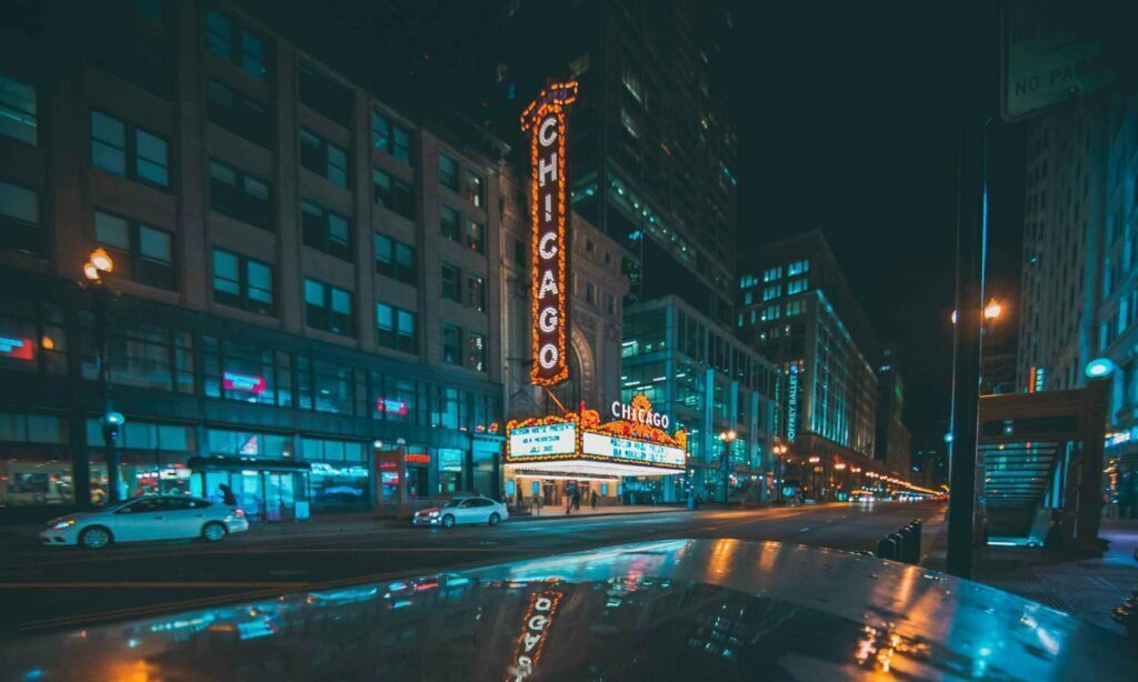 Illuminated Chicago city street with iconic theatre sign reflecting on wet pavement at night.